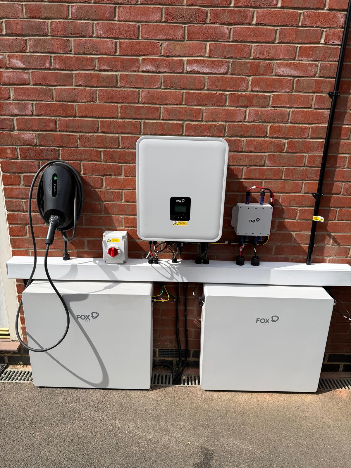 A Fox ESS inverter, two battery units and a myenergi Zappi charger mounted along an outside wall