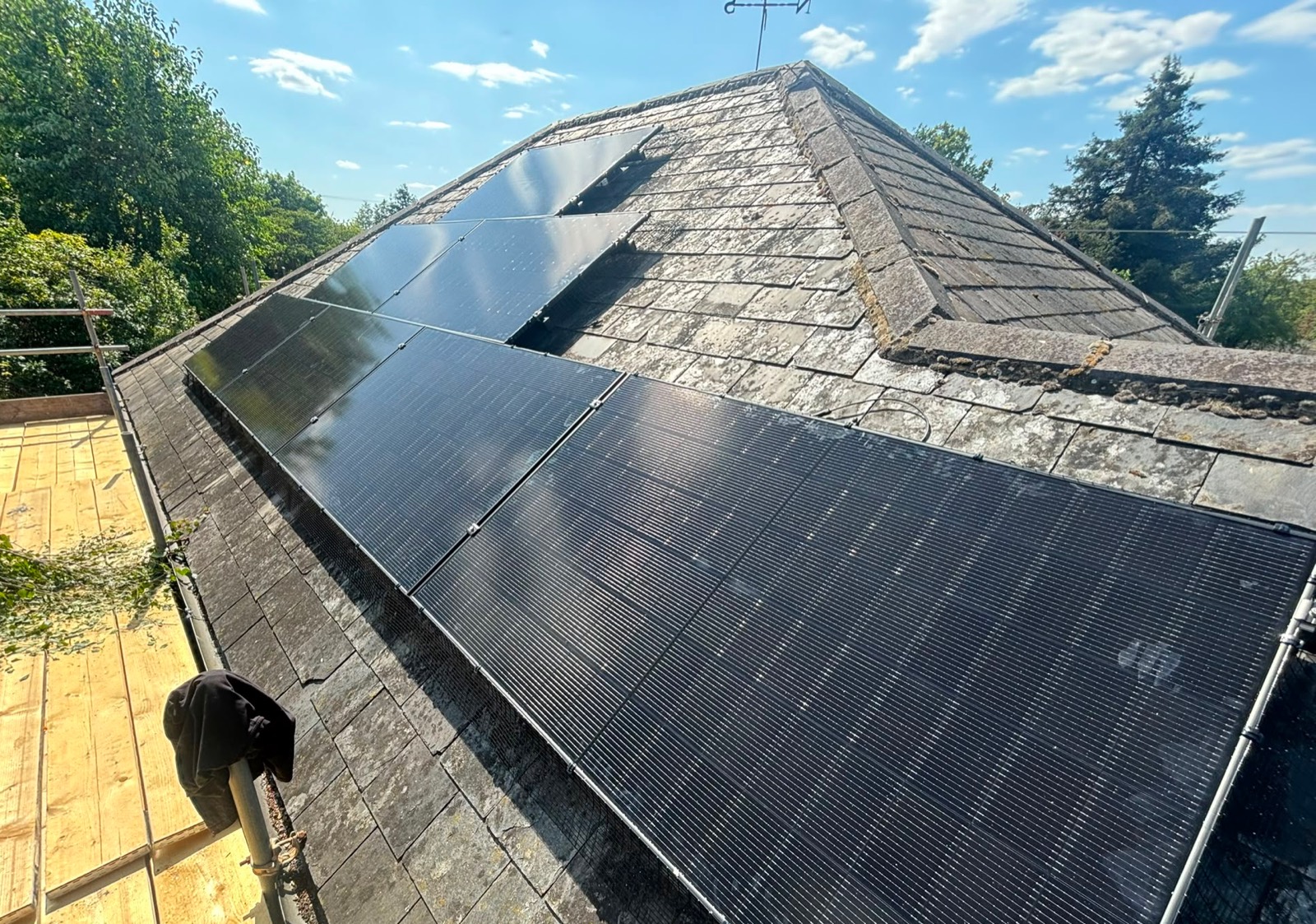 Solar panels on a slate roof seen from the scaffold, with a second array on the adjoining pitch