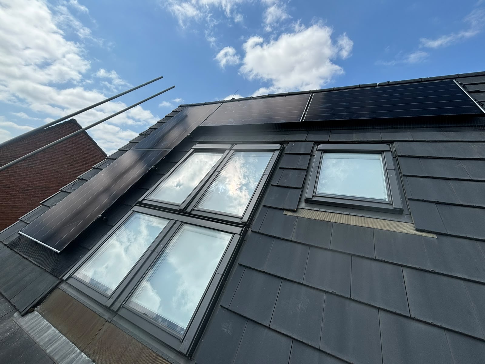 Black solar panels fitted around roof windows on a steep tiled roof