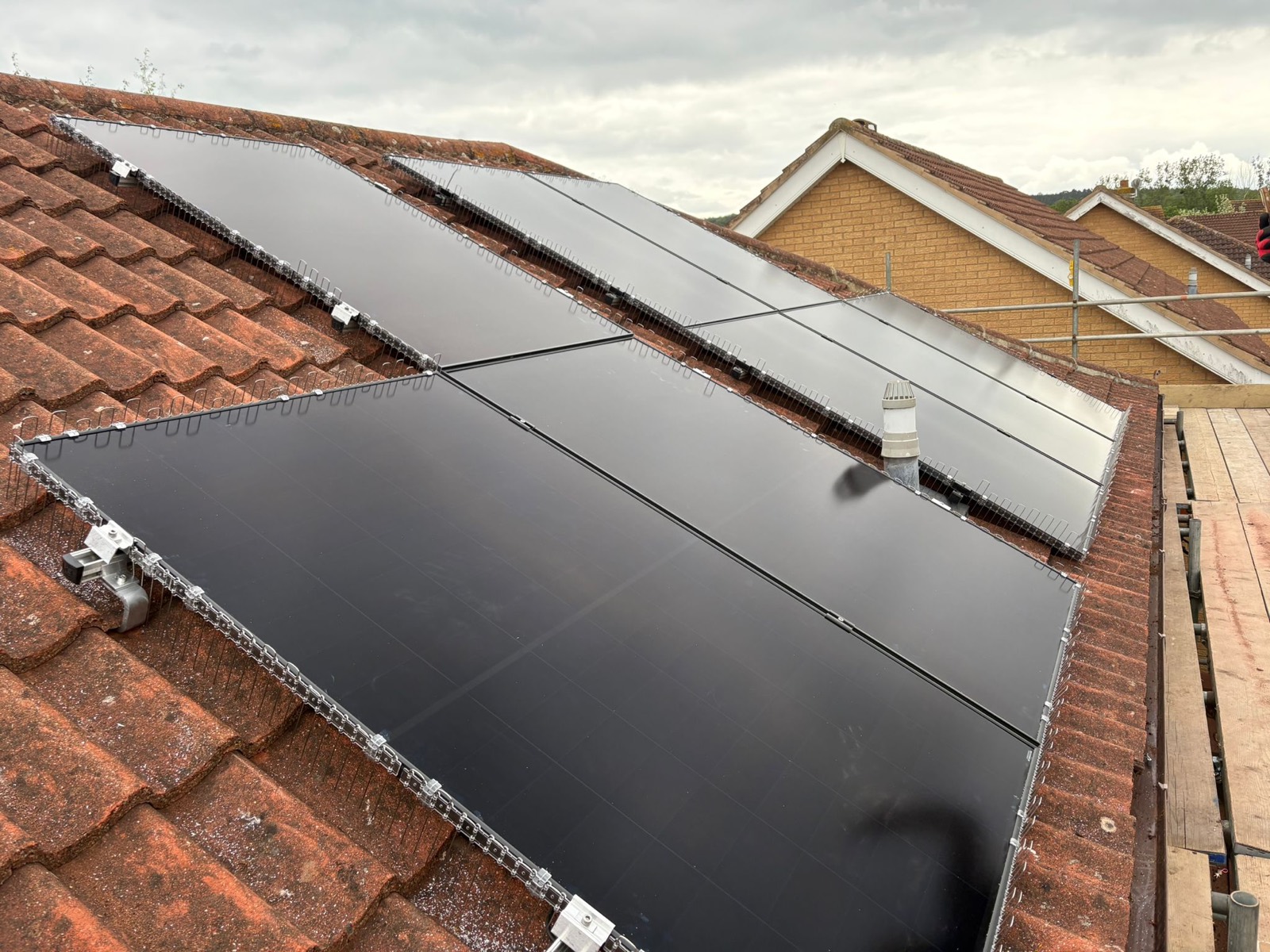 Close-up of solar panel mounting rails and bird mesh along the edge of a tiled roof