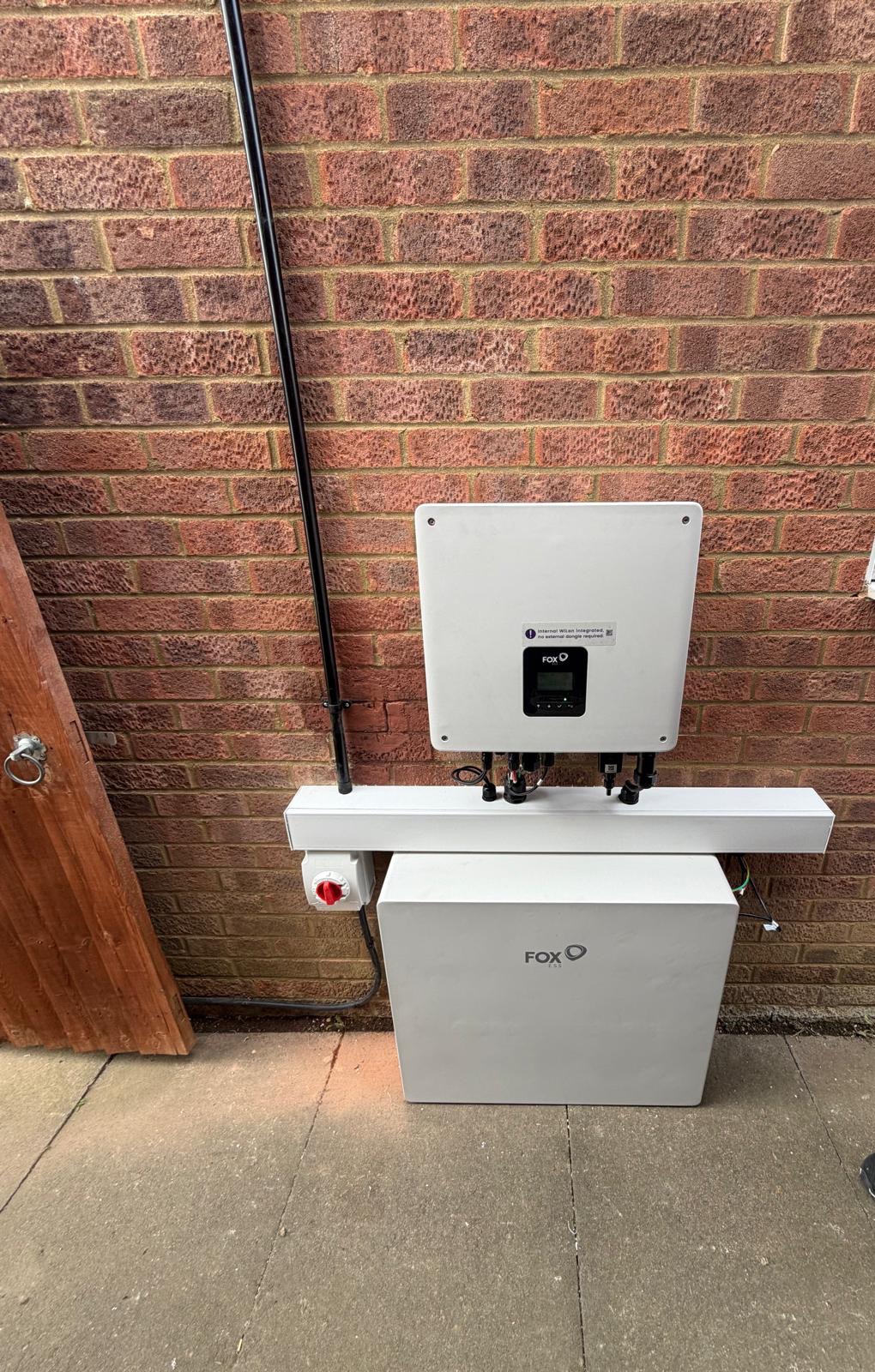 A Fox ESS hybrid inverter above a floor-standing battery on an outside wall
